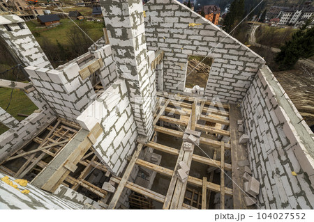 Interior of future cottage, energy saving walls of large white hollow foam insulation blocks and temporary wooden scaffolding frame. Construction, masonry, modern technology concept. 104027552