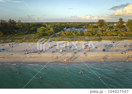 High angle view of crowded Nokomis beach in Sarasota County, USA. Many people enjoing vacations time swimming in ocean water and relaxing on warm Florida sun at sundown High angle view of crowded Nokomis beach in Sarasota County, USA. Many people enjoing vacations time swimming in ocean water and relaxing on warm Florida sun at sundown 104027587