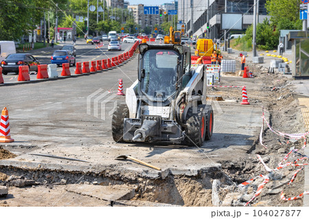 Repair of the carriageway of the city road, compact and powerful construction equipment on the background of the city street being repaired. 104027877