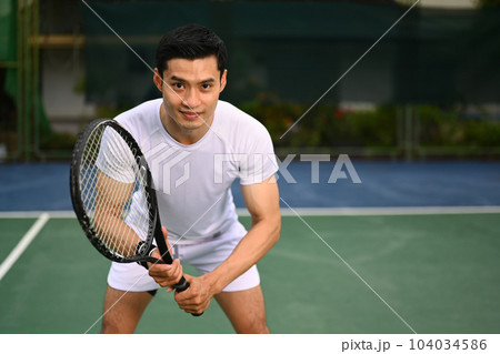 Focused male tennis player crouching in ready position and holding racket while waiting for serving ball from competitor Focused male tennis player crouching in ready position and holding racket while waiting for serving ball from competitor 104034586