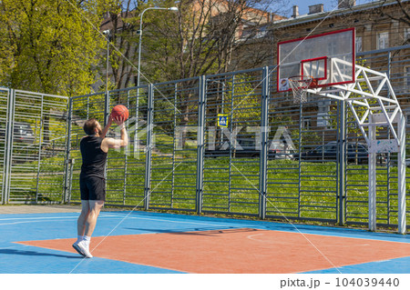 Athletic man in sportswear playing basketball game, successfully throws ball into the basket ring Athletic man in sportswear playing basketball game, successfully throws ball into the basket ring 104039440