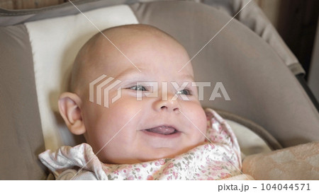 Closeup Newborn Child Sits in the Baby Girl Car Seat. Cute New Born Baby in Car Seat. Cute Little Kid Happy Smile Sitting on Baby Stroller Carriage Seat. Portrait. Face. 104044571
