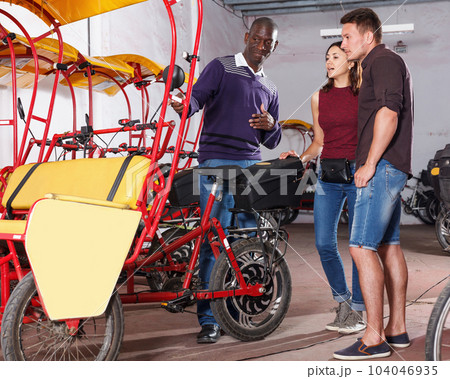 Smiling African-American man bikecab driver talking to couple Smiling African-American man bikecab driver talking to couple 104046935