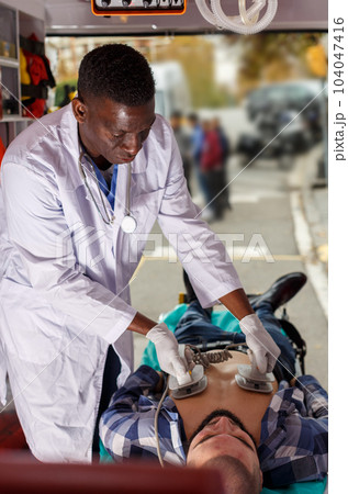 Doctor resuscitating patient with help of defibrillator 104047416