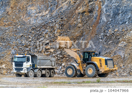 an excavator is loading a truck with stone at a quarry 104047966