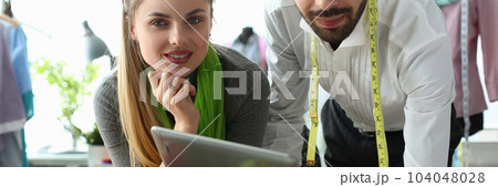Man and woman designers are discussing new collection of clothes on digital tablet in workshop Man and woman designers are discussing new collection of clothes on digital tablet in workshop 104048028