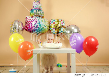 A small child for a birthday near a birthday cake on the background of balloons. A small child for a birthday near a birthday cake on the background of balloons. 104049596