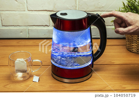 man turns off the heating button of a modern glass electric kettle man turns off the heating button of a modern glass electric kettle 104050719