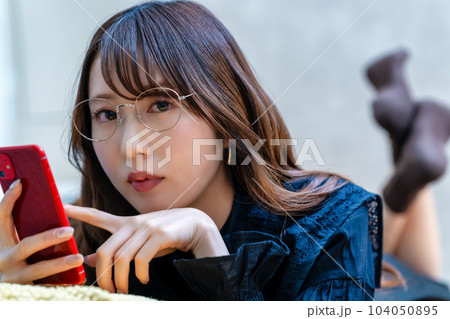 寝転んでスマホを使う眼鏡の女性 寝転んでスマホを使う眼鏡の女性 104050895