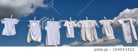 children's white clothes hanging on a rope on clothespins on the street against  104053422