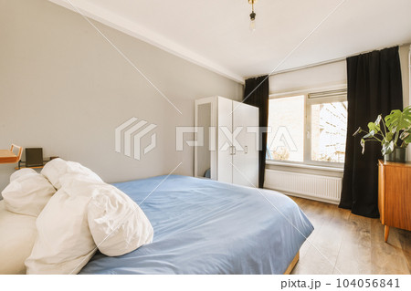 a bedroom with a bed, dresser and plant in the corner on the right side of the room is empty 104056841