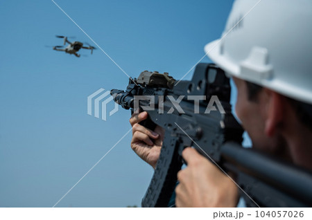 Caucasian man in a helmet shoots a flying drone with a rifle. Caucasian man in a helmet shoots a flying drone with a rifle. 104057026