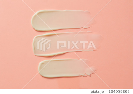 Flat lay of three streaks of cream with an opaque white texture are brushed against a pastel pink background.  Facial creme, foam, gel or body lotion skincare icon.  104059803