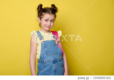 Caucasian emotional doubtful little kid girl 6 years old, primary school student, pupil with pink backpack, dressed in casual blue denim and yellow t-shirt, isolated on yellow color studio background Caucasian emotional doubtful little kid girl 6 years old, primary school student, pupil with pink backpack, dressed in casual blue denim and yellow t-shirt, isolated on yellow color studio background 104060162