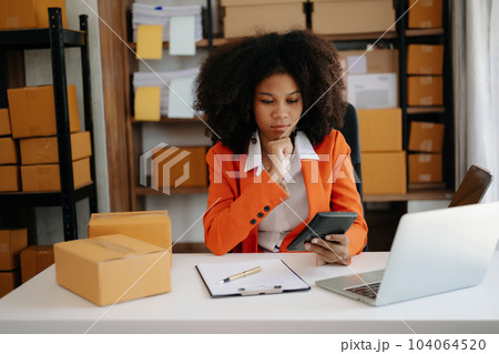 Startup small business SME, Entrepreneur owner African woman using smartphone or tablet taking receive and checking online purchase shopping order to preparing pack product box. .. Startup small business SME, Entrepreneur owner African woman using smartphone or tablet taking receive and checking online purchase shopping order to preparing pack product box. .. 104064520