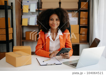 Startup small business SME, Entrepreneur owner African woman using smartphone or tablet taking receive and checking online purchase shopping order to preparing pack product box. .. Startup small business SME, Entrepreneur owner African woman using smartphone or tablet taking receive and checking online purchase shopping order to preparing pack product box. .. 104064521