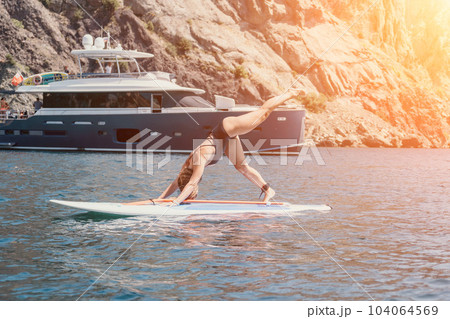 Woman sea sup. Close up portrait of happy young caucasian woman with long hair looking at camera and smiling. Cute woman portrait in bikini posing on sup board in the sea 104064569