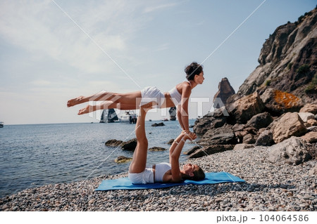 Woman sea yoga. Two Happy women meditating in yoga pose on the beach, ocean and rock mountains. Motivation and inspirational fit and exercising. Healthy lifestyle outdoors in nature, fitness concept. Woman sea yoga. Two Happy women meditating in yoga pose on the beach, ocean and rock mountains. Motivation and inspirational fit and exercising. Healthy lifestyle outdoors in nature, fitness concept. 104064586