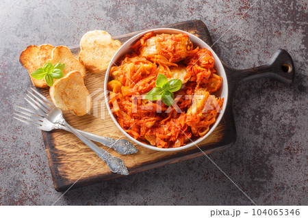 White fish stew with carrots and onions in spicy tomato sauce served with toast close-up on a wooden board. horizontal top view White fish stew with carrots and onions in spicy tomato sauce served with toast close-up on a wooden board. horizontal top view 104065346