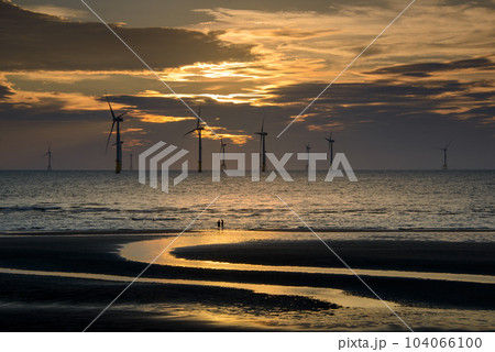 Fans of wind turbines spin over the sparkling sea. Dynamic clouds at sunset. 104066100