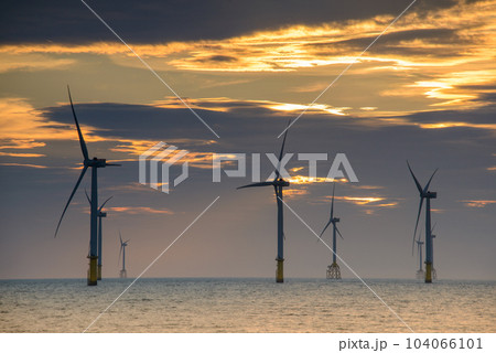 Fans of wind turbines spin over the sparkling sea. Dynamic clouds at sunset. Fans of wind turbines spin over the sparkling sea. Dynamic clouds at sunset. 104066101
