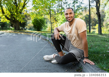 Portrait of successful mature adult hispanic man during jogging and jogging active physical exercise resting in park sitting on grass smiling and looking at camera. 104066353