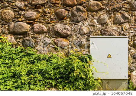 Electrical control cabinet against a rough stone wall 104067048