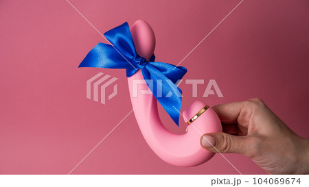 Woman holding curved dildo with blue ribbon on pink background. Copy space.  104069674
