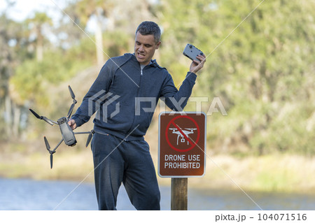 Drone operator is disappointed because he isn't allowed to fly his quadcopter in national park no drone area. Man is unable to use his UAV near restriction notice sign. Airspace use regulations Drone operator is disappointed because he isn't allowed to fly his quadcopter in national park no drone area. Man is unable to use his UAV near restriction notice sign. Airspace use regulations 104071516