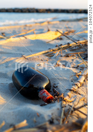 夕方の砂浜に捨てられたお酒のボトル 104072524