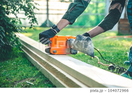 The man grinds the boards with a belt grinder, the electric tool for grinding and polishing the surface of the wooden board. 104072966