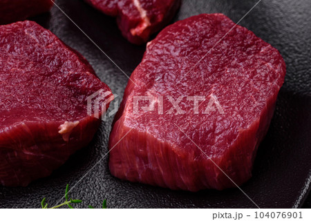 Juicy raw beef with spices, salt and herbs on a dark concrete background 104076901
