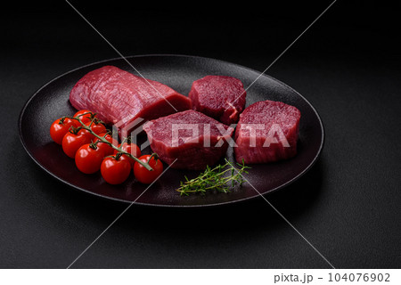 Juicy raw beef with spices, salt and herbs on a dark concrete background 104076902
