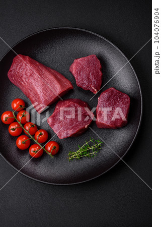 Juicy raw beef with spices, salt and herbs on a dark concrete background Juicy raw beef with spices, salt and herbs on a dark concrete background 104076904