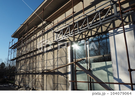 Scaffolding on a new one-story house. Facade works. Building bussiness. Low-rise private building. Plastering the wall of a building. Shop building. Metal production structures 104079064