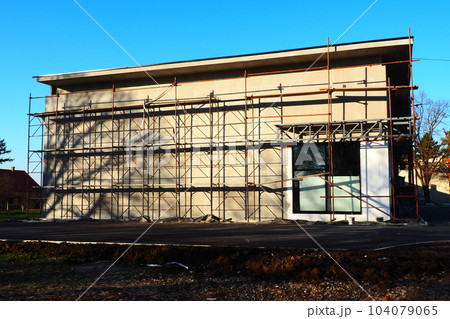Scaffolding on a new one-story house. Facade works. Building bussiness. Low-rise private building. Plastering the wall of a building. Shop building. Metal production structures 104079065