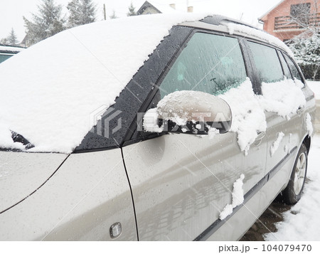 Snow and ice on the windshield, retrovisors and rear-view mirrors of the car. Winter driving conditions. Snow cleaning. Road traffic in winter. Metallic car. Snowdrifts and slush 104079470
