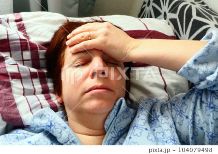 Sick woman in bed. Headache, runny nose and cold. Paleness of the face and faintness of the body. Feeling unwell. The patient holds his forehead with his hand and covers his eyes. Sick woman in bed. Headache, runny nose and cold. Paleness of the face and faintness of the body. Feeling unwell. The patient holds his forehead with his hand and covers his eyes. 104079498