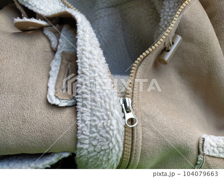 Suede outerwear. Overhead loops for buttons. Open zipper. Beige faux suede with sheepskin on the fold of a demi-season garment. seams in the material. Clothing industry and fashion 104079663