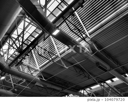 The roof of a hangar, a production hall or a sports hall. Metal structures, beams, supporting elements. Ventilation systems in large halls and rooms. Skylights. Industrial interior 104079720