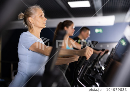 Older sportswoman training at elliptical machine in gym Older sportswoman training at elliptical machine in gym 104079828