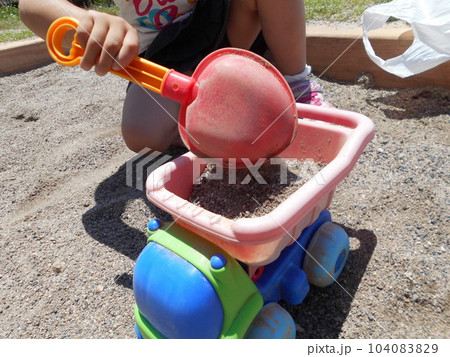 公園の砂場でダンプカーの玩具とスコップで遊ぶ子供の手元 104083829