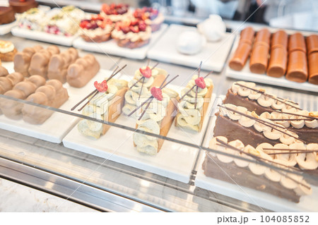 A variety of cakes covered with chocolate and decorated with pistachio mousse. A showcase in a pastry shop with delicious desserts with fresh berries and cream. Delicious pastries in the coffee shop. 104085852