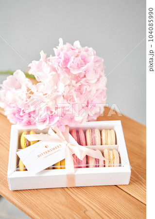 Dessert French Macarons in present box. Sweet dessert on a flowers background. Still life with macaroni cakes and different flower. Delivery concept, coffee and flower shop 104085990