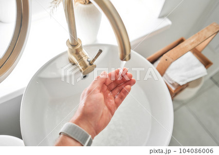 Hand washing with faucet over the washbasin in modern bathroom. Rotary nozzle on the mixer to adjust the flow of water. White bathroom sink for washing hands Hand washing with faucet over the washbasin in modern bathroom. Rotary nozzle on the mixer to adjust the flow of water. White bathroom sink for washing hands 104086006