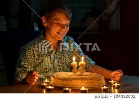 Happy blond little kid boy celebrating his birthday. Preteen child blowing candles on homemade baked cake, indoor. Birthday party for school children, family celebration 104092002