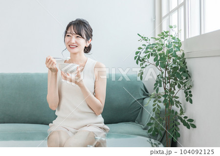 家のソファでヨーグルト・乳製品を食べるアジア人女性（ビフィズス菌・乳酸菌・乳製品・腸活） 104092125