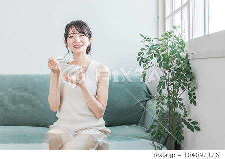 家のソファでヨーグルト・乳製品を食べるアジア人女性（ビフィズス菌・乳酸菌・乳製品・腸活） 104092126