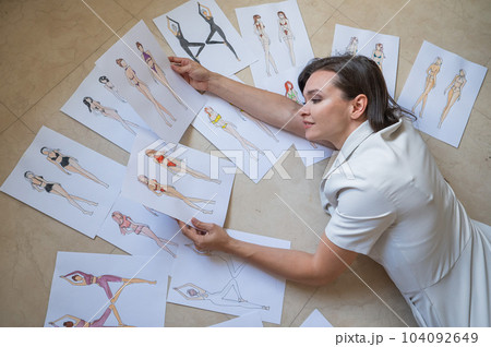 A woman lies on the floor and looks at sketches of swimwear and underwear.  104092649