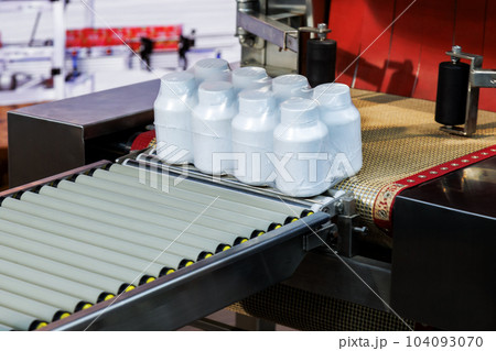 pharmaceutical and medicine white plastic bottles are wrapping in transparent plastic film on conveyor belt at packing machine in the cosmetic and supplement manufacturing. pharmaceutical and medicine white plastic bottles are wrapping in transparent plastic film on conveyor belt at packing machine in the cosmetic and supplement manufacturing. 104093070